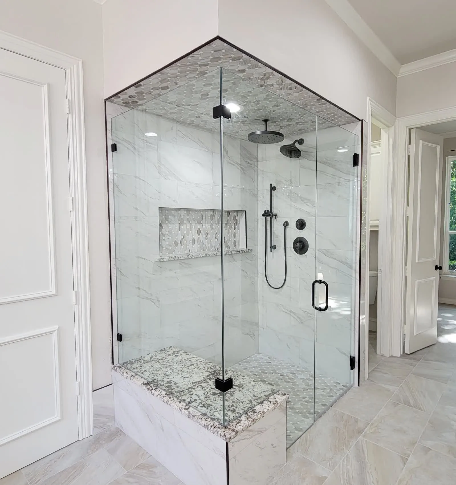 After: the same corner rebuilt as a frameless glass shower with pebble-mosaic accent tile
